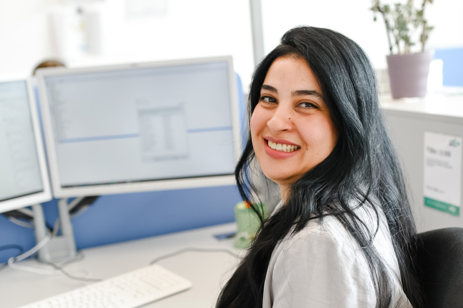 Eine Mitarbeiterin der IT-Betrieb sitzt an ihrem Schreibtisch und schaut über die Schulter in die Kamera.