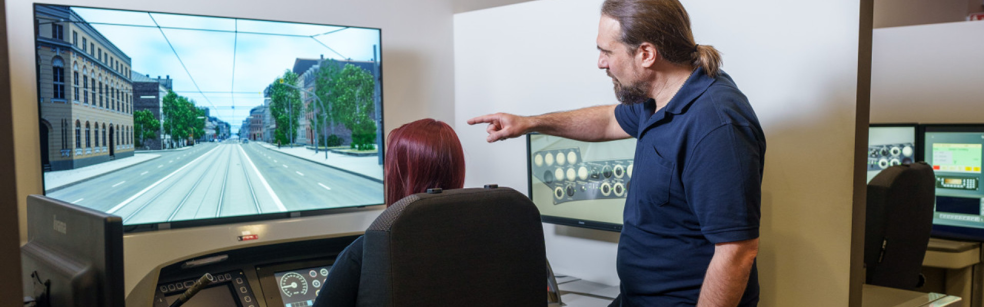 Ein Ausbildungsleiter erklärt einer künftigen Fahrerin etwas am Bahnfahrsimulator.