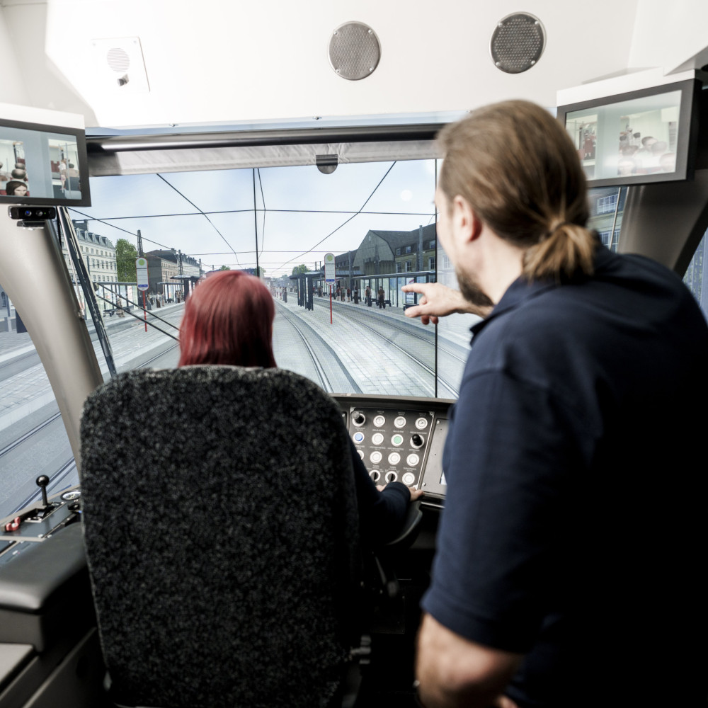 Ein Ausbildungsleiter erklärt einer künftigen Fahrerin etwas am Bahnfahrsimulator.