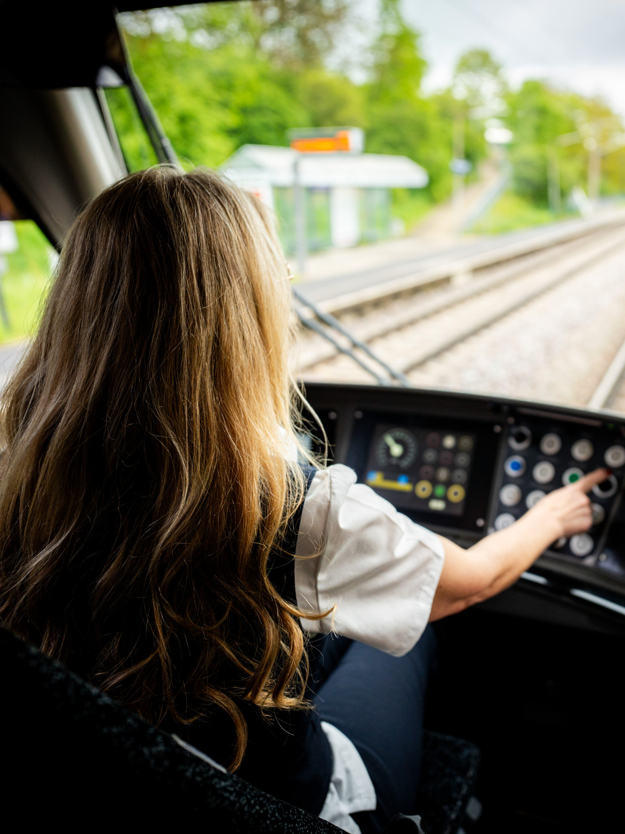 Eine Mitarbeiterin (von hinten) fährt eine Bahn mit Blick in die Landschaft. 