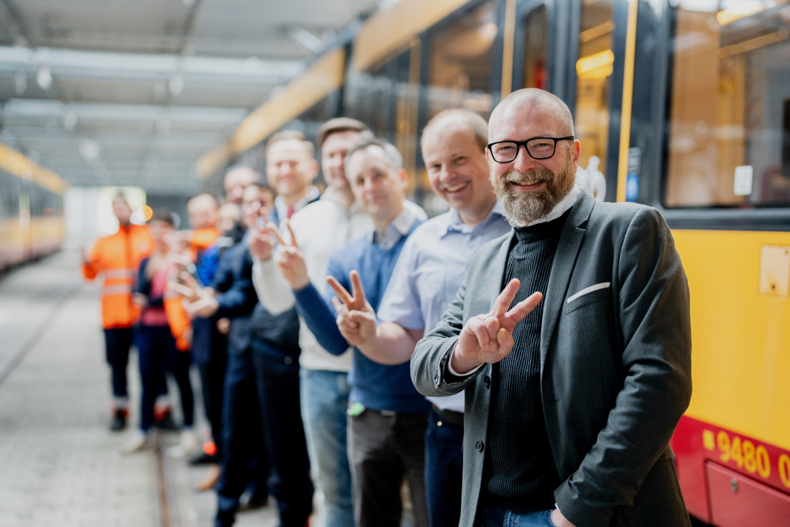 Einige Mitarbeiter stehen mit der #TeamV Pose an einer Bahn schräg versetzt nach hinten.